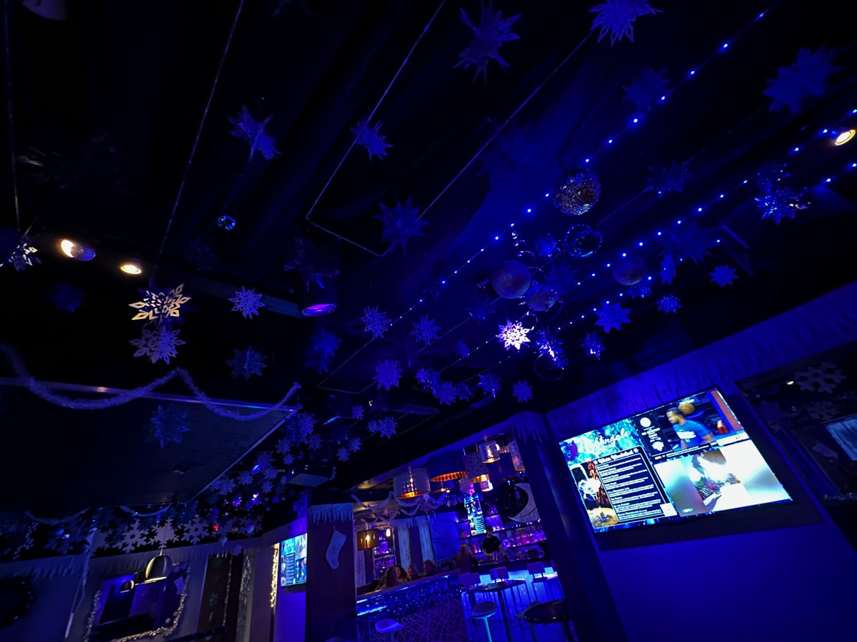 Blue holiday lights, hanging snowflakes, and ornaments above the bar at Nightingale Cocktail