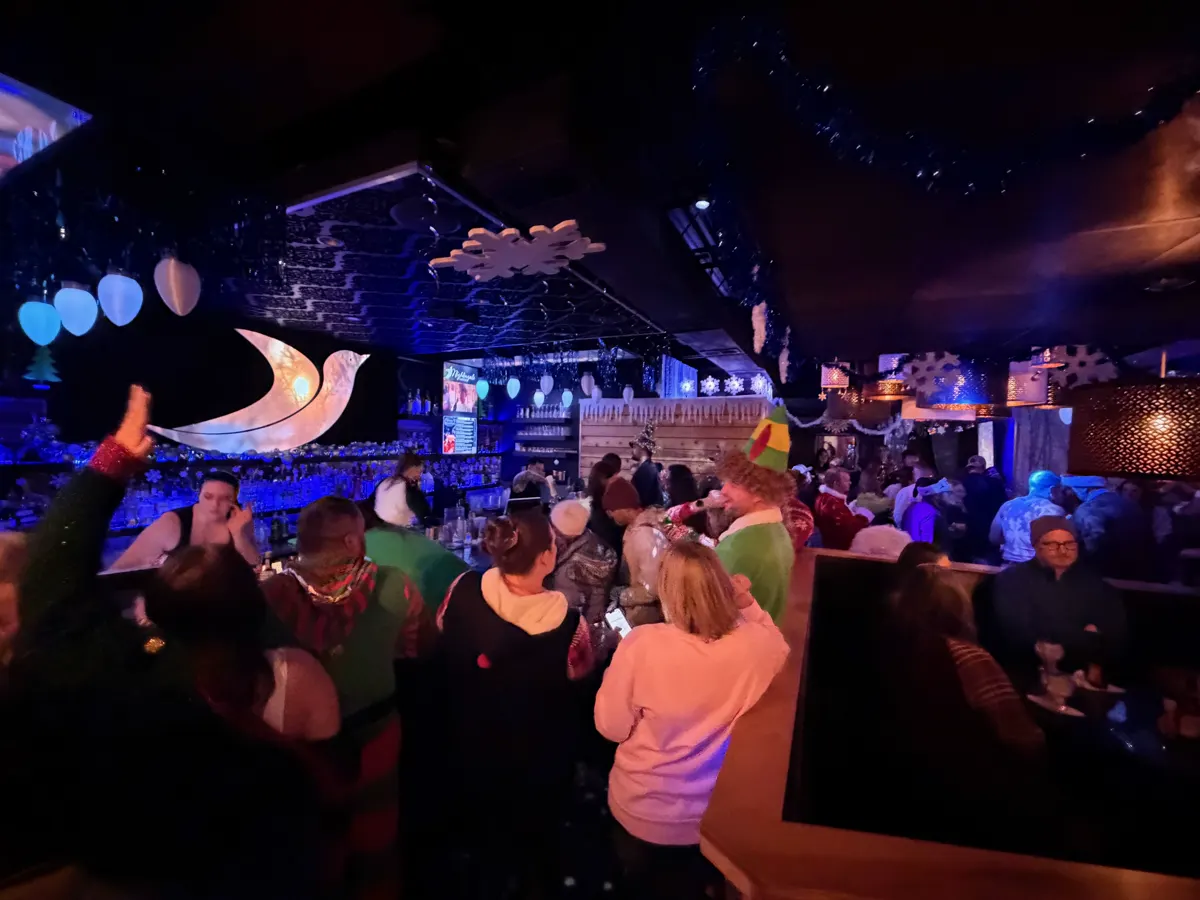 Guests in festive outfits gathered at Nightingale Cocktail beneath blue holiday lights and hanging snowflakes