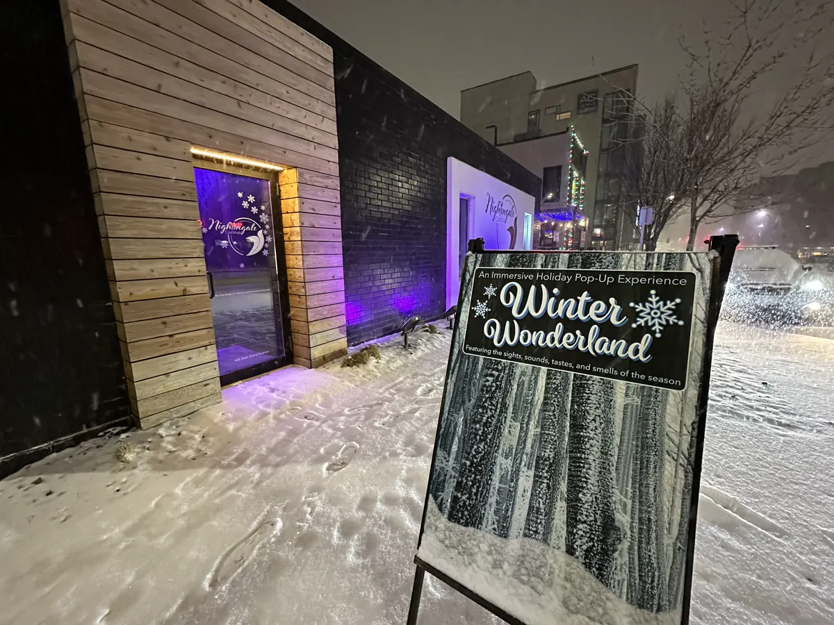 Nightingale Cocktail’s entrance lit in purple beside the Winter Wonderland sidewalk sign on East Grand Avenue